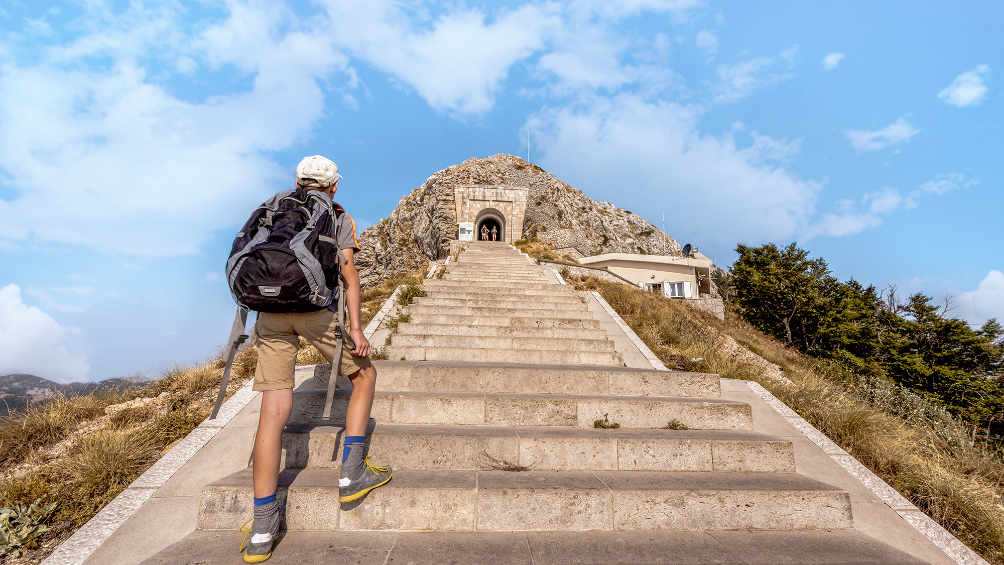 Young tourist boy  with backpack climbing the steep stairs to Njegusi mausoleum in Lovcen National Park, Montenegro