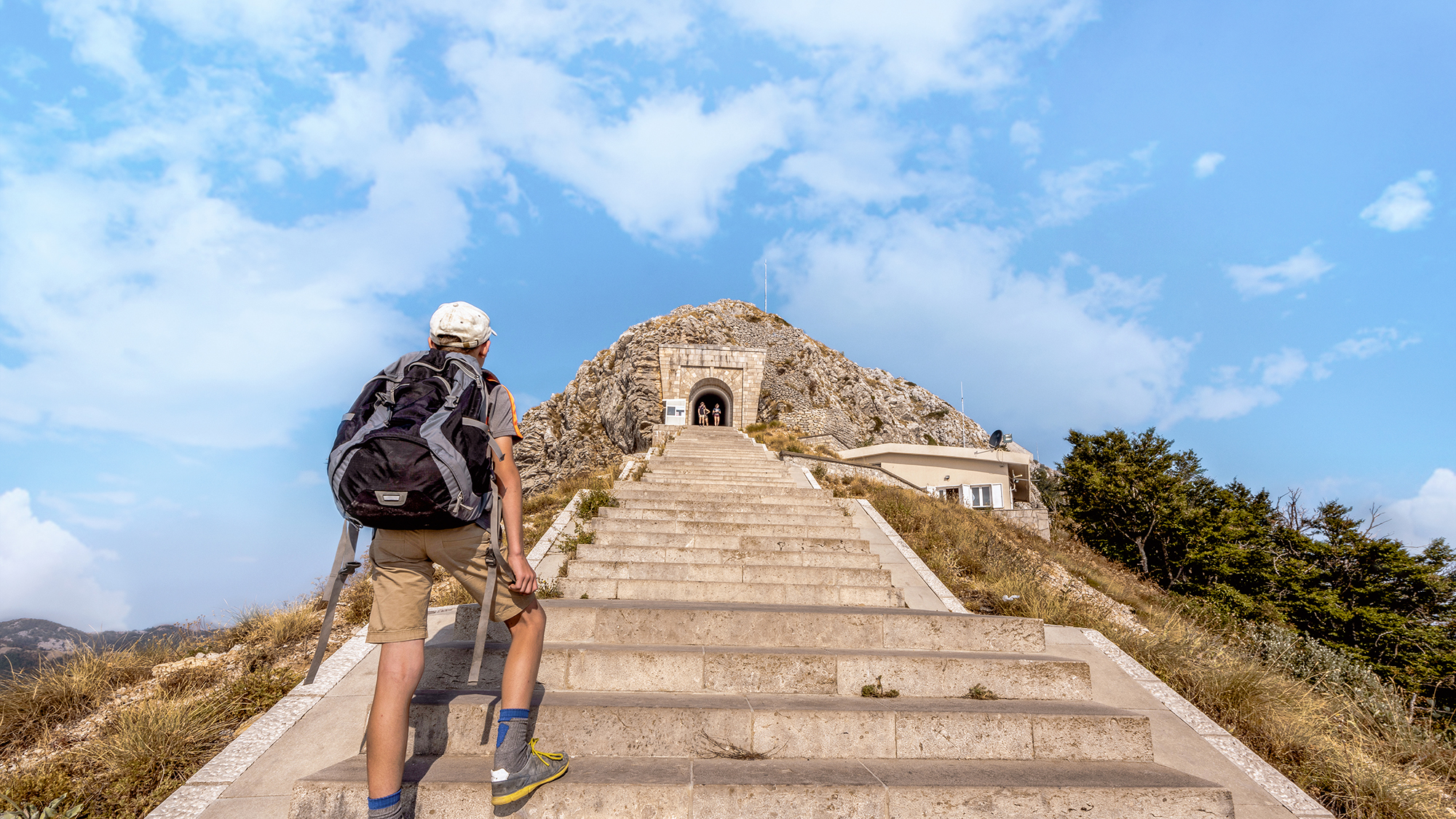 Young tourist boy  with backpack climbing the steep stairs to Njegusi mausoleum in Lovcen National Park, Montenegro